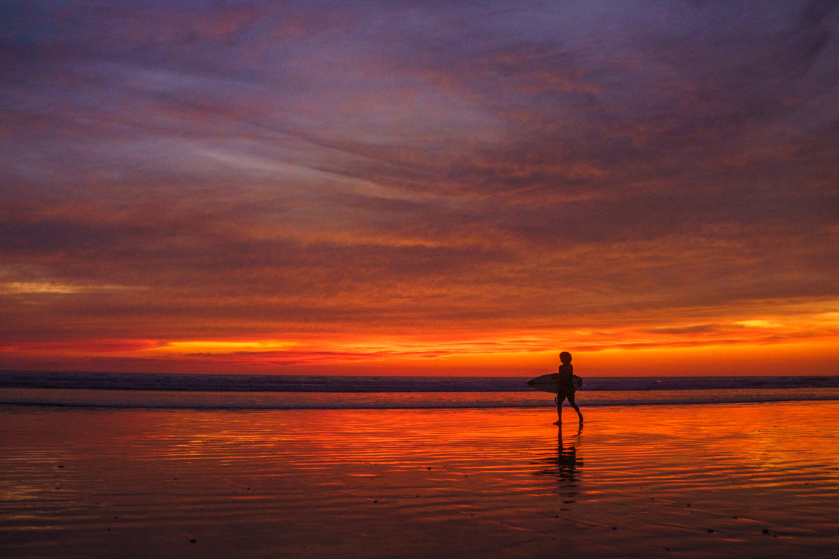 a surfer walks in the sunset glow at our destination retreat in Costa Rica